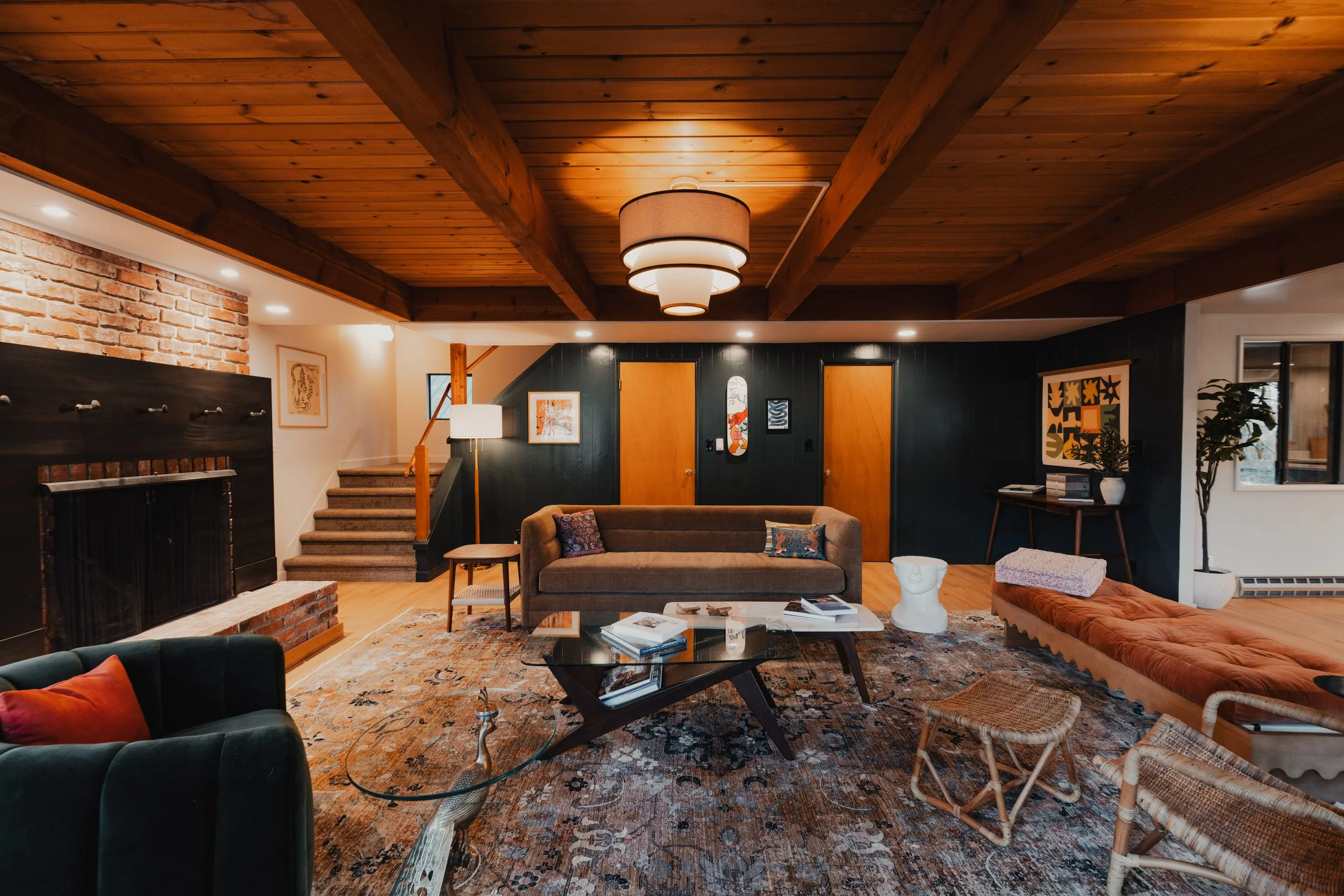 Living room with a wooden ceiling, brick fireplace, modern art, brown sofa, glass coffee table, and woven chairs.