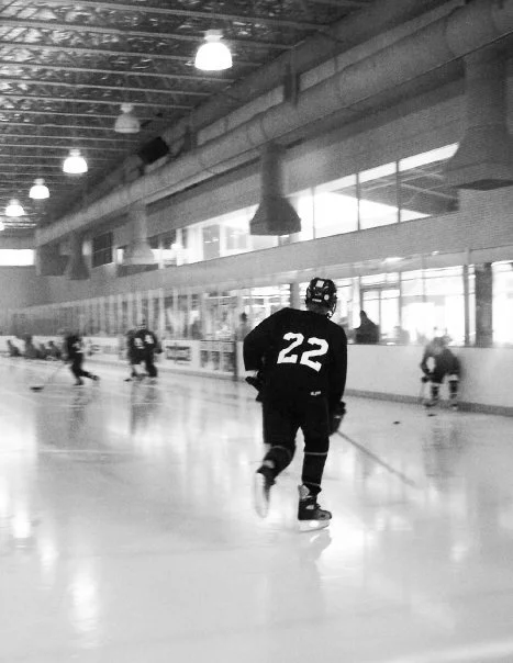 Hockey players practicing on an indoor ice rink with one player skating towards the camera, wearing jersey number 22.