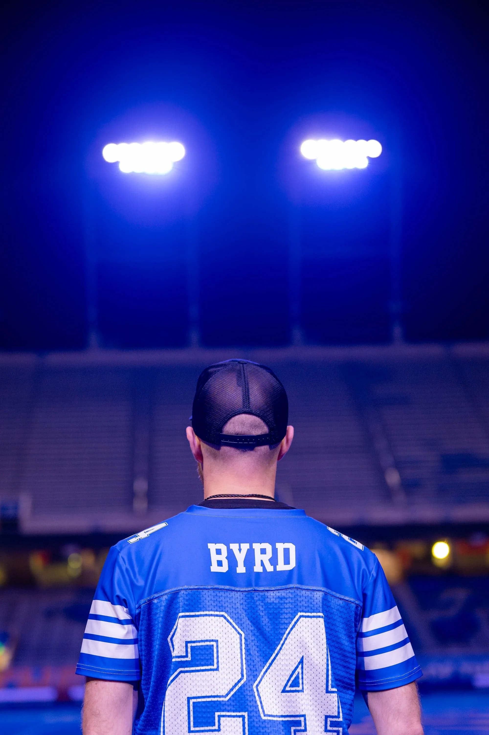 A man wearing a blue football jersey with the name 'BYRD' and number '24' is standing in a stadium, facing away, under bright stadium lights.