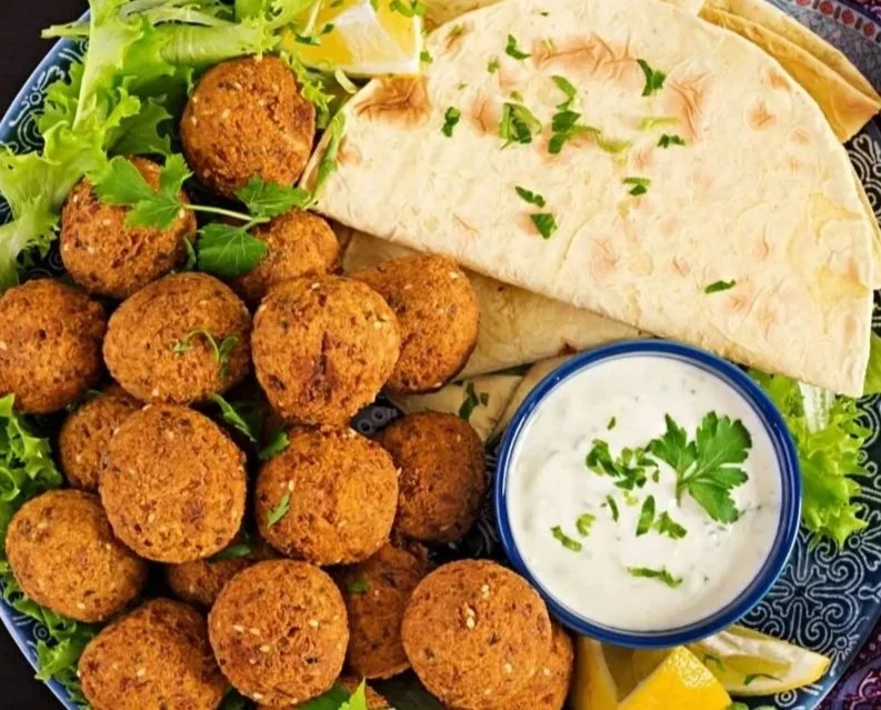 Plate of falafel balls with hummus, pita bread, lemon wedges, and fresh greens.