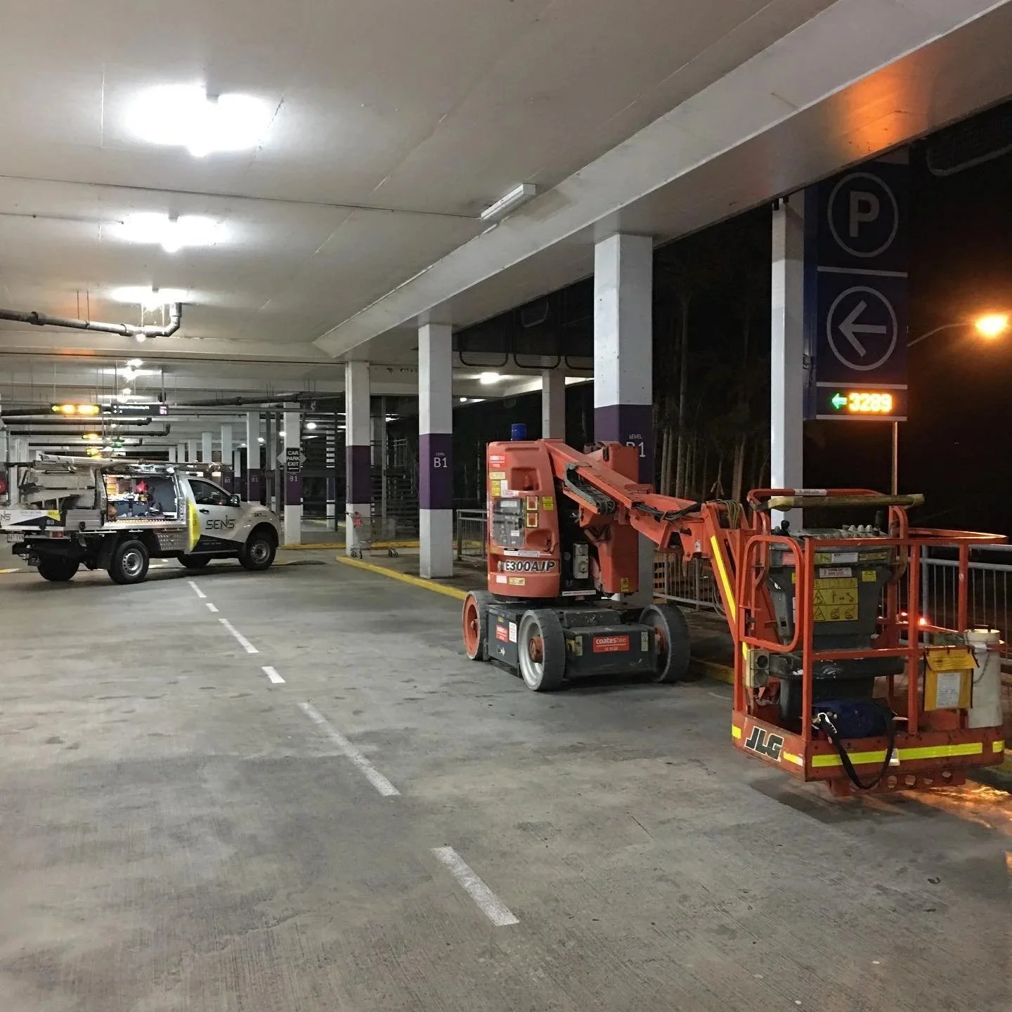A parking garage at night with maintenance equipment including a cherry picker and a utility truck.