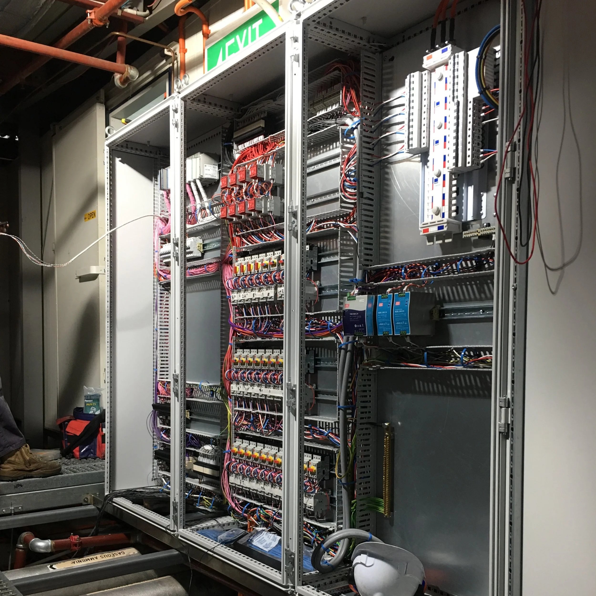 An open electrical control panel with wires, circuit breakers, and components inside.