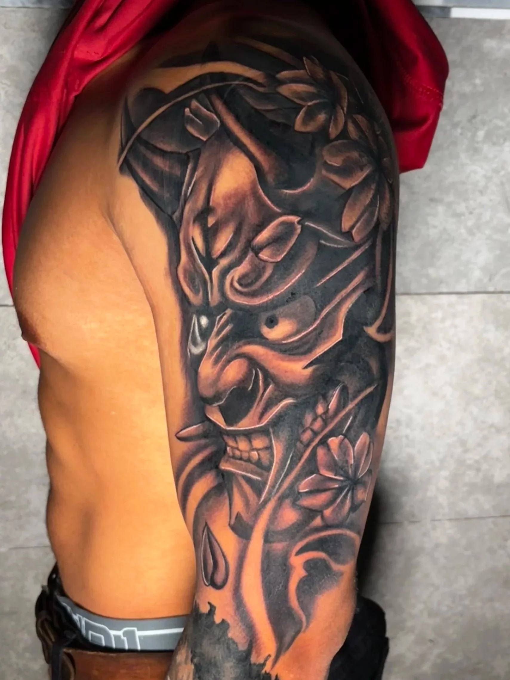 Close-up of a person's upper arm tattoo of a hanya mask with black and grey shading.