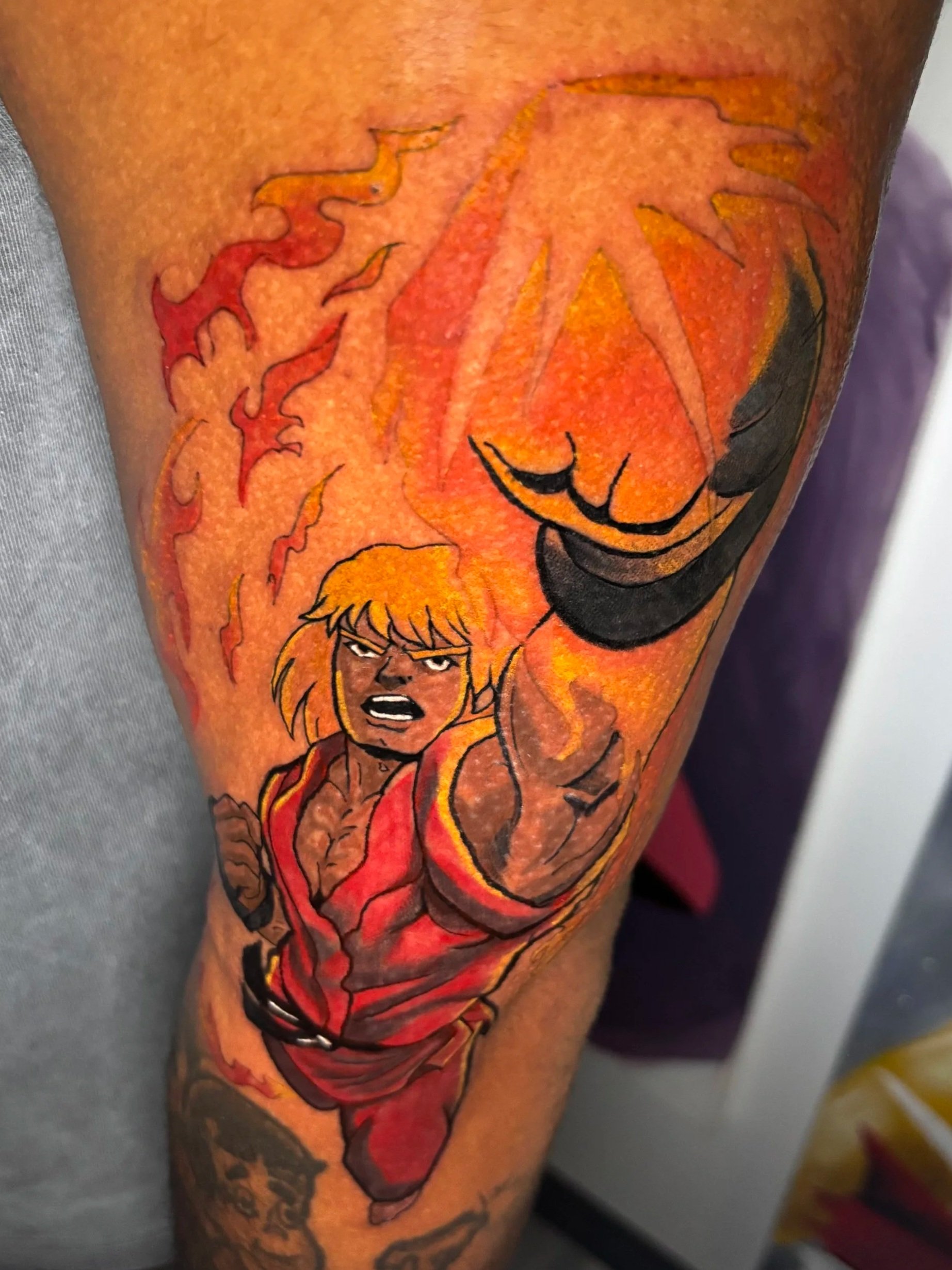A colorful tattoo of Ken Masters from Street Fighter with his fist extended, wearing a red karate gi, on a person's arm. Video game. color