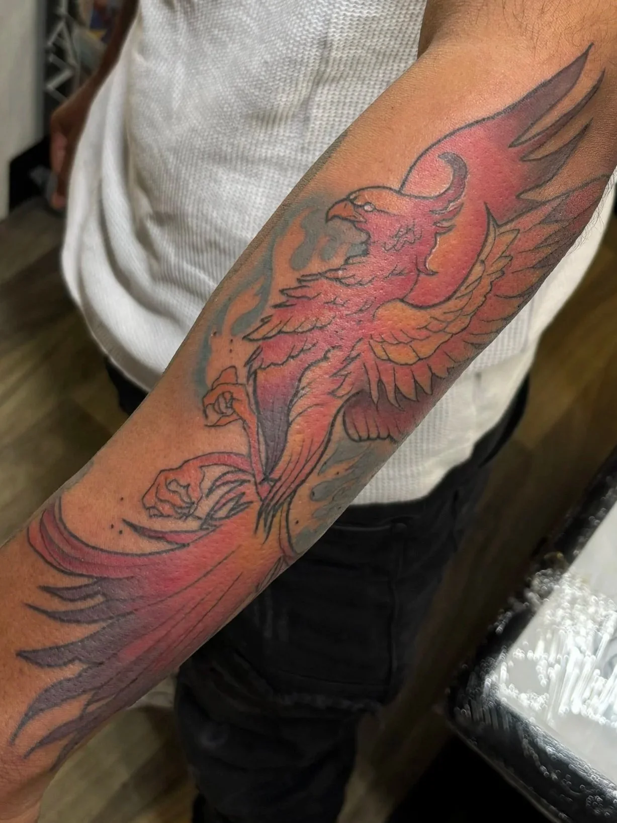 Tattoo artist working on a person's arm, which has a new tattoo of a fiery red and orange phoenix with black outlines and flames.