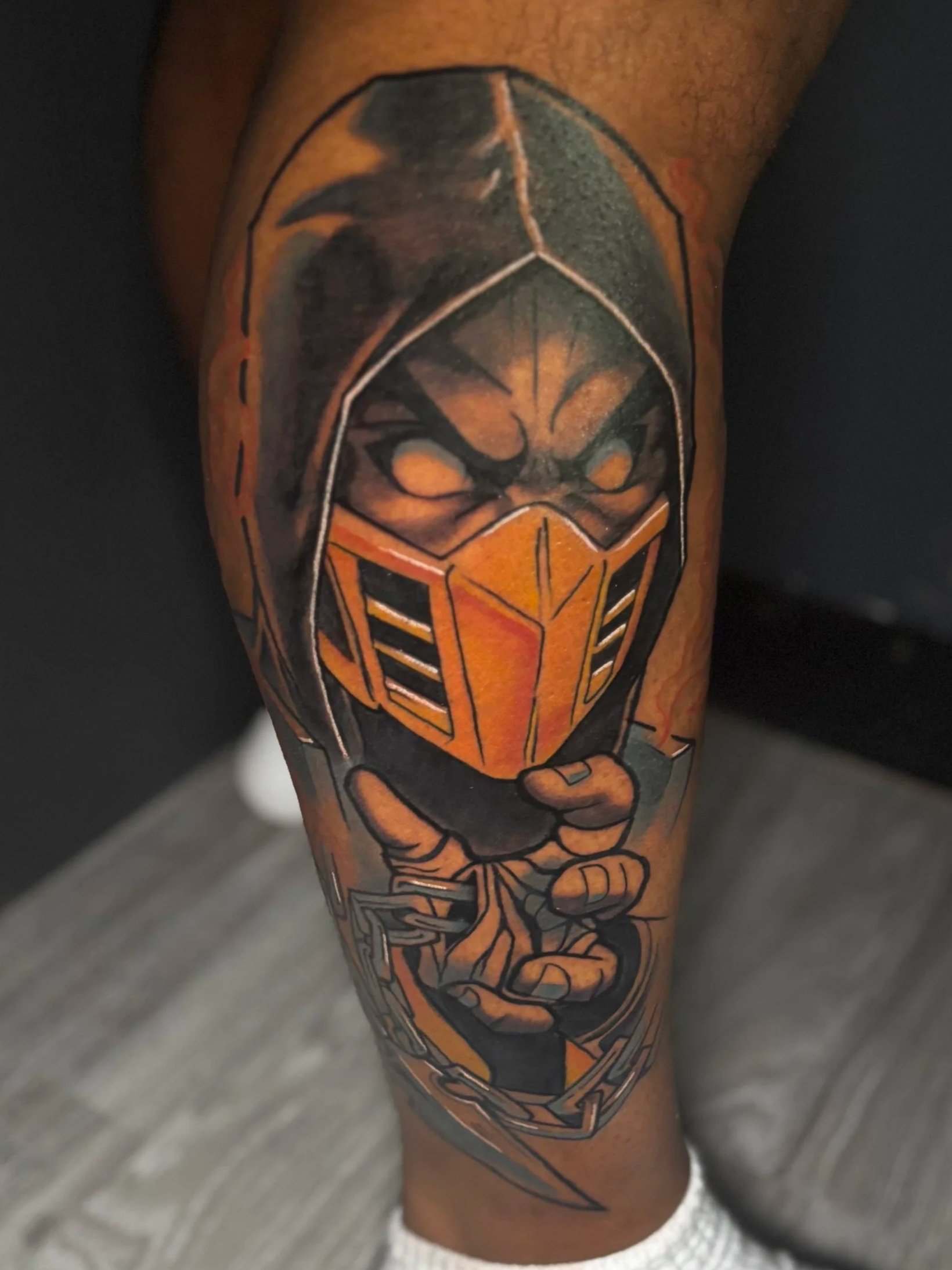 A tattoo of Scorpion from Mortal Combat, depicted with flames and bold lines, on a person's leg.