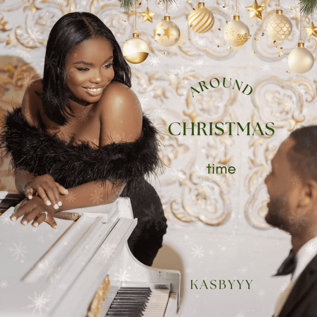 A woman in a black dress with a feathered stole leaning over a white piano, smiling at a man in a suit and glasses, with Christmas ornaments hanging above and festive gold and white decor in the background. Text on the image says 'Around Christmas time KasbYYY.'