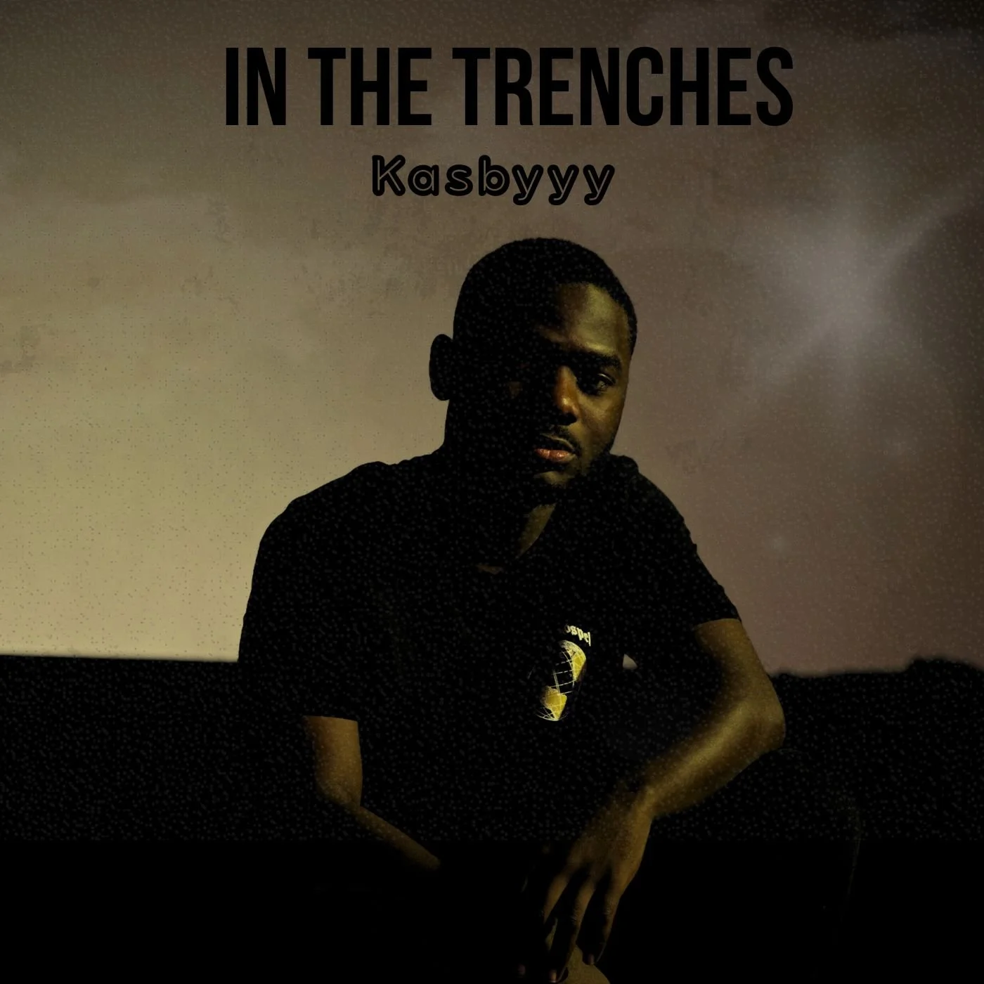 A young man in dark clothing with a graphic T-shirt is sitting outdoors at night, under a cloudy sky. Text at the top reads 'In the Trenches' and 'Kasbyyy' is written below.