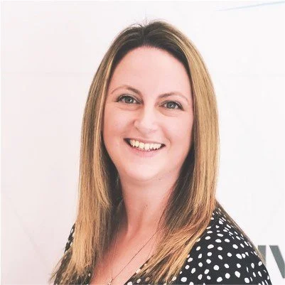 Smiling woman with long light brown hair wearing a black and white polka dot top.