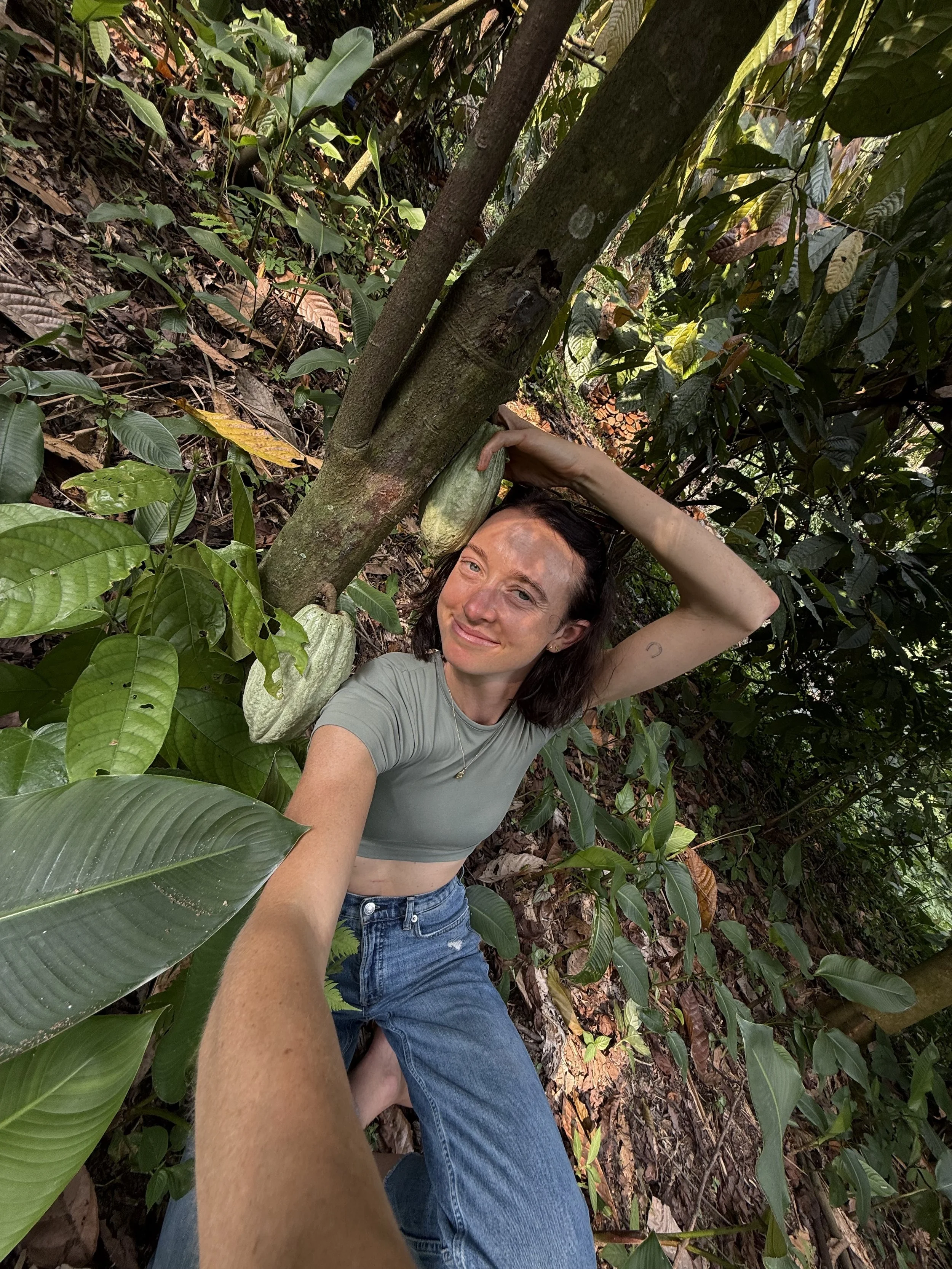 Kris, founder of Cacao for Beings, photographed in nature near cacao trees, reflecting her connection to ceremonial cacao and its origins