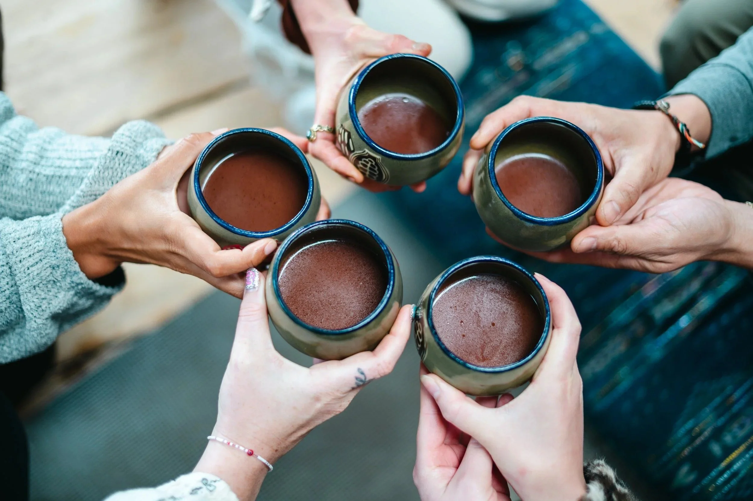 Five people holding ceramic mugs filled with hot chocolate or coffee, clinking them together in a celebration or toast.