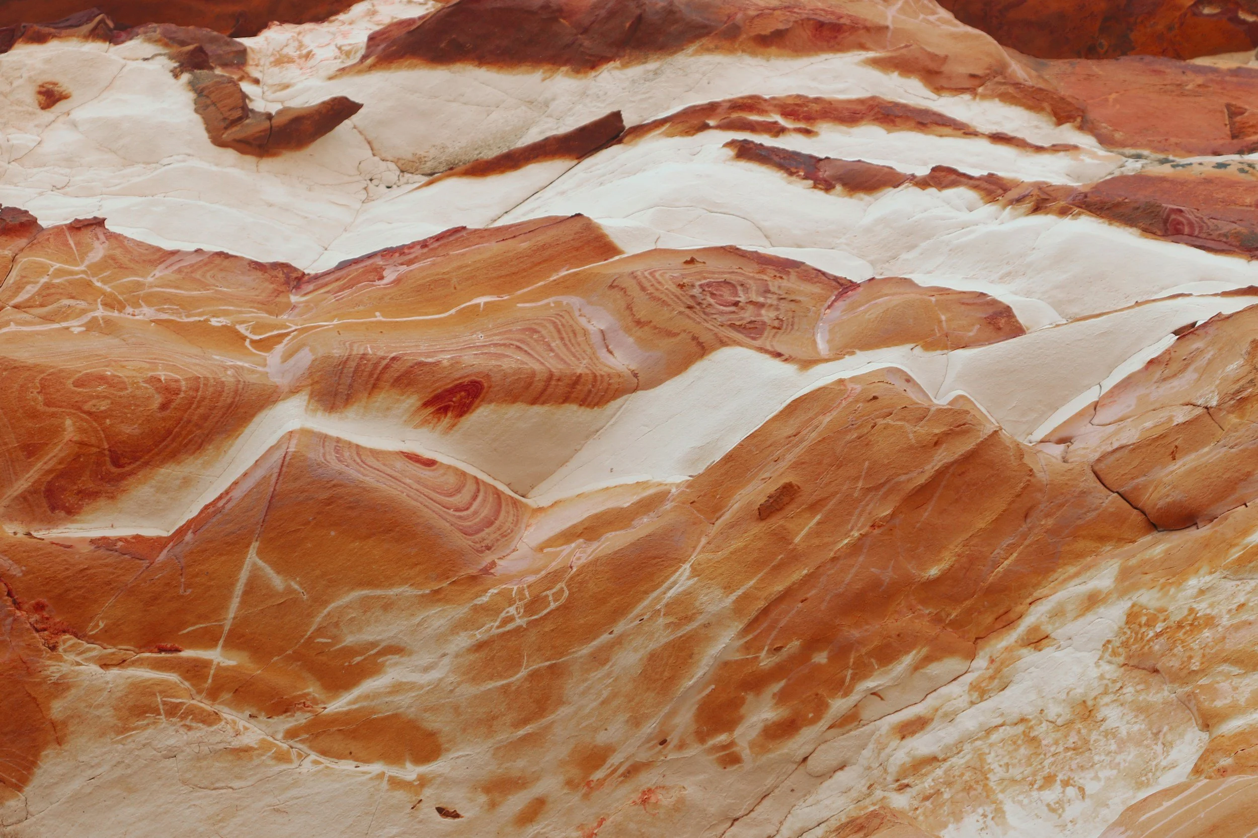 Close-up of red, white, and beige layered rock formations with wavy patterns.