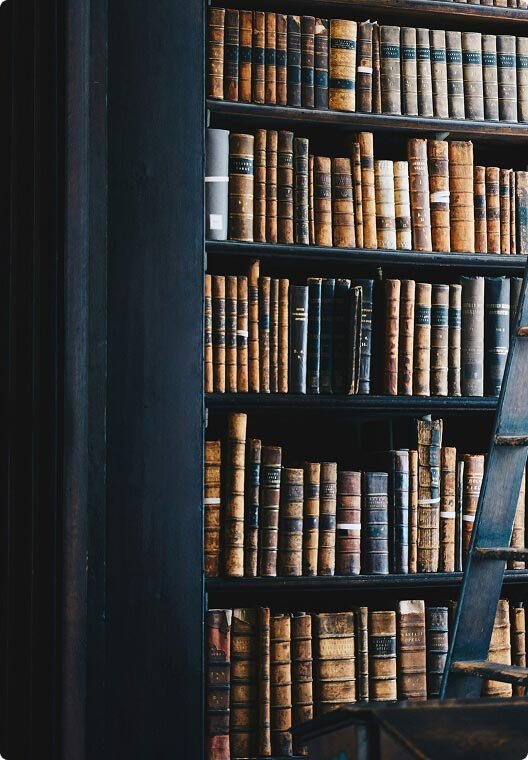 Old leather-bound books on black wooden bookshelves in a library or study.