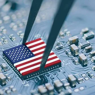 Microchip with an American flag on it being handled with tweezers on a circuit board.