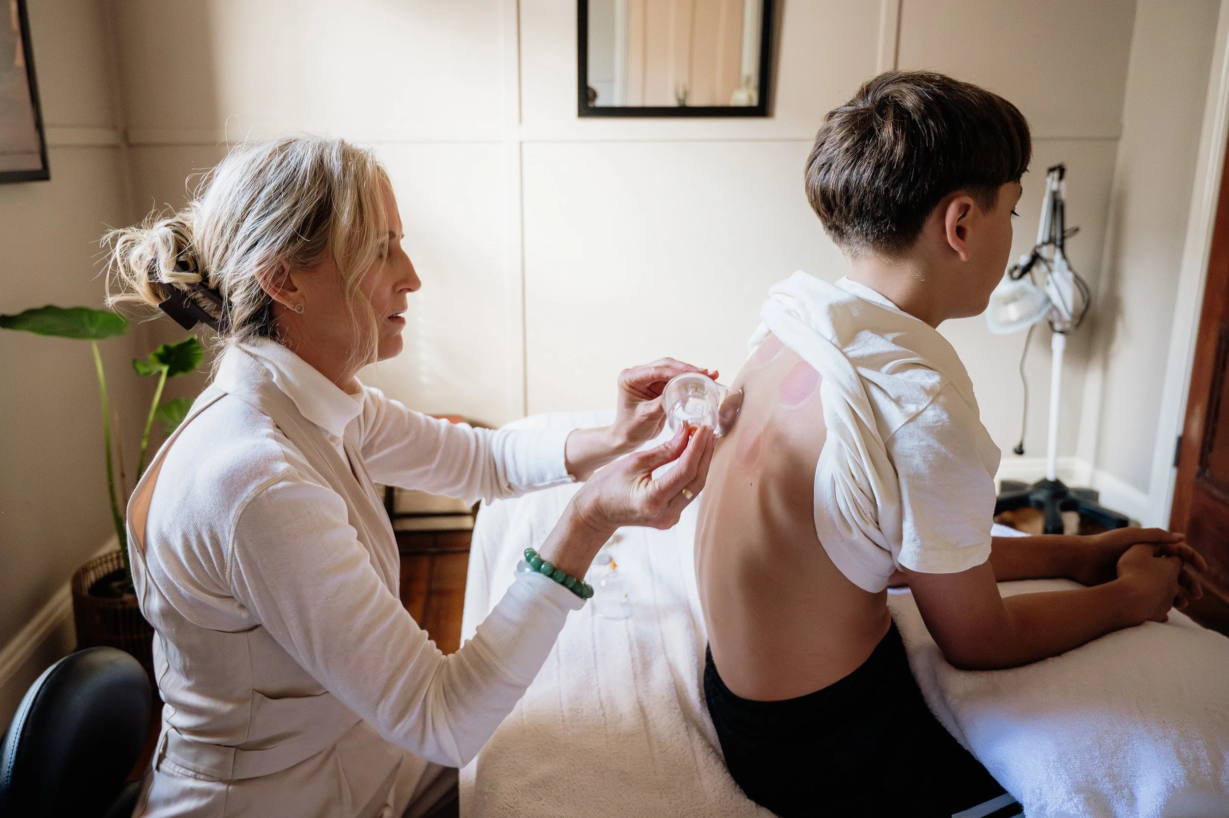 A woman a healthcare worker administering a flu shot to a young man sitting on an examination table.