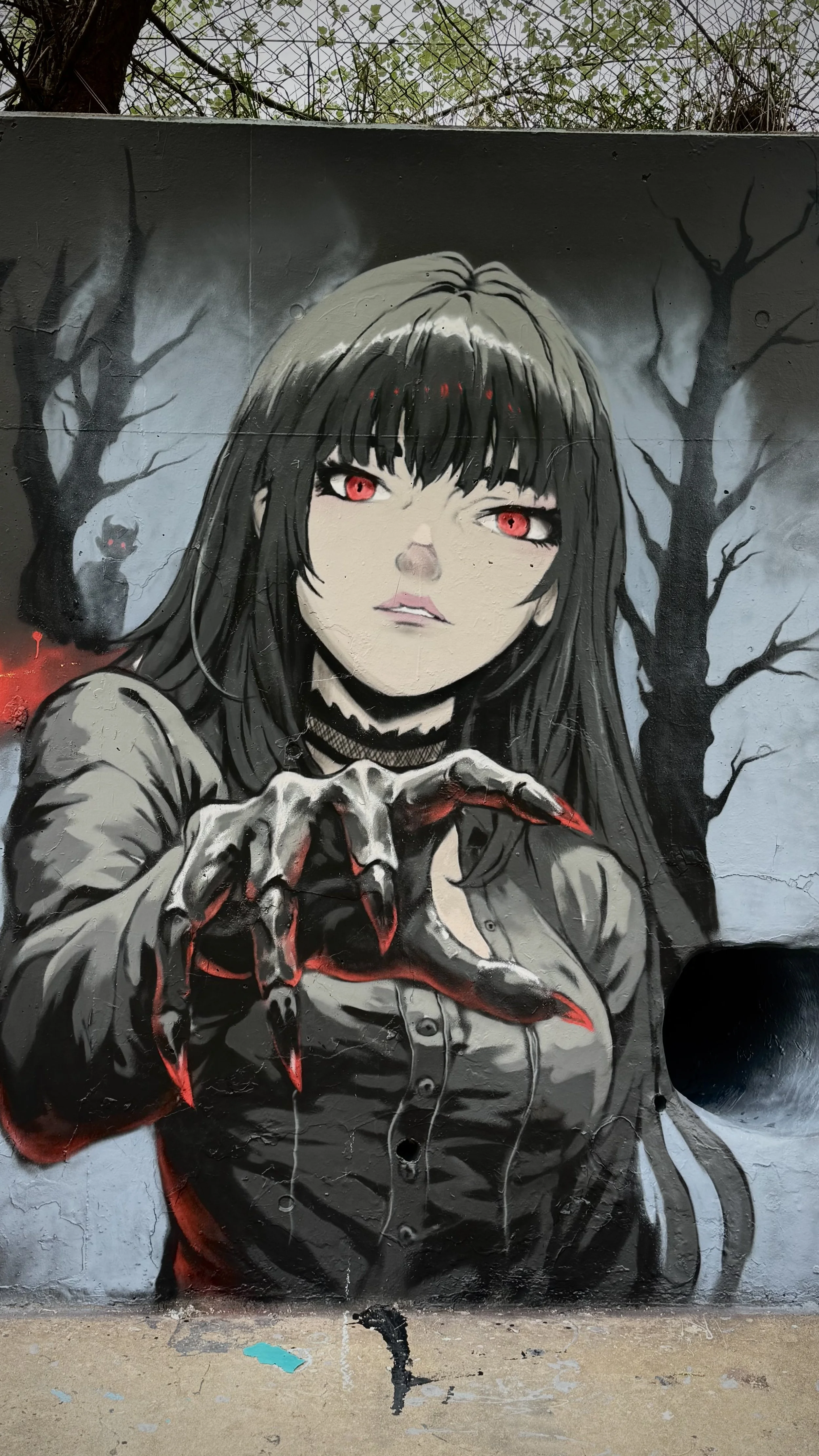 Graffiti art of a woman with black hair and red eyes, reaching out with clawed, red-tipped fingers, with dark leafless trees and a black cat in the background.
