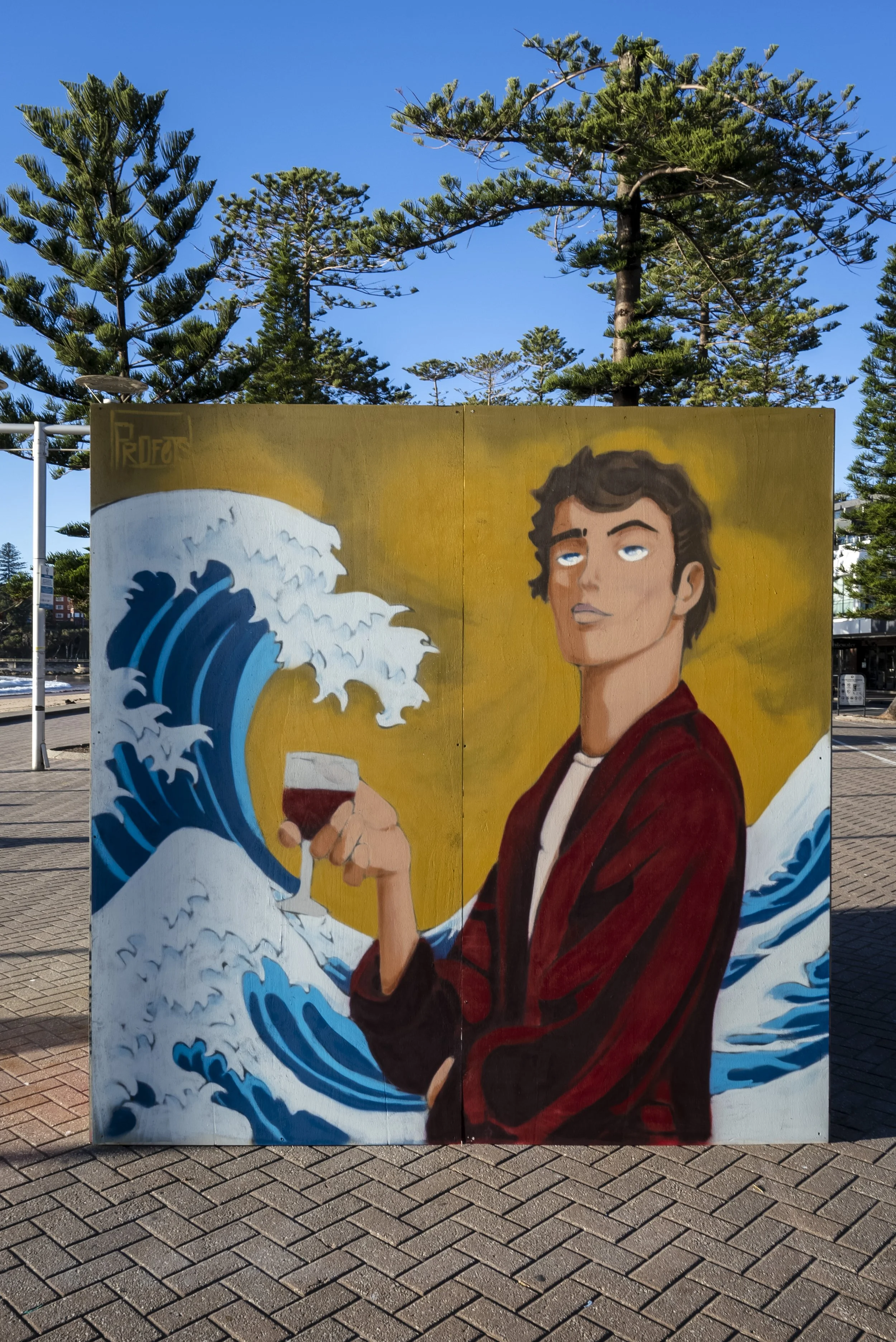 Street art mural featuring a young man with dark hair, wearing a red jacket, holding a glass of red wine, with a background of stylized ocean waves and a bright yellow sky.