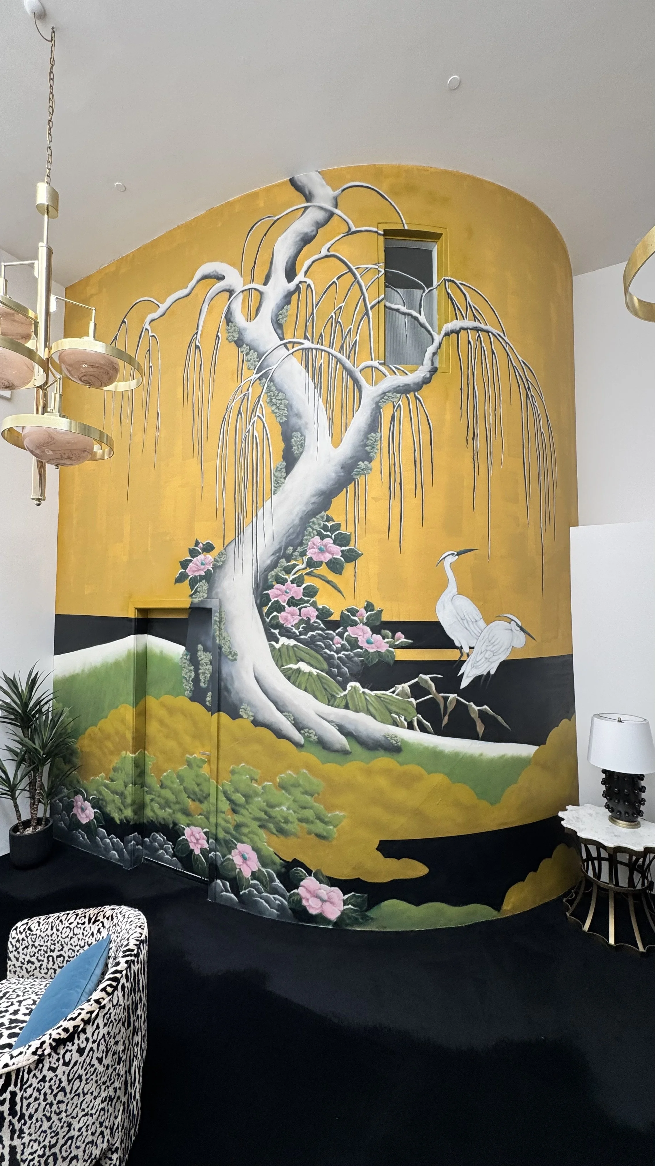 Interior with a large, decorative wall mural of a Japanese-inspired scene featuring a weeping cherry tree, pink flowers, green foliage, two white cranes, and a gold background.