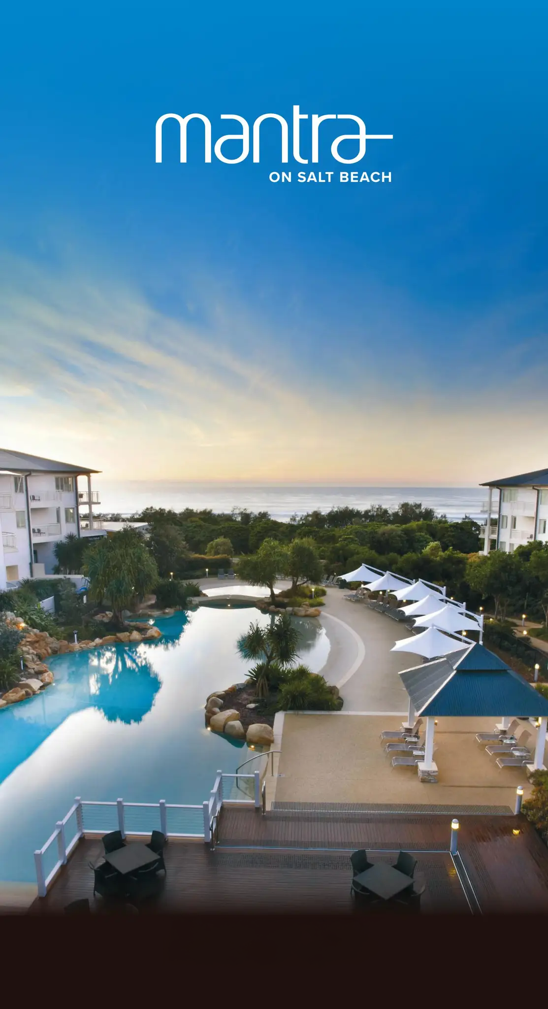 Resort's pool area with lounge chairs, umbrellas, and landscaped surroundings overlooking the ocean at sunset.