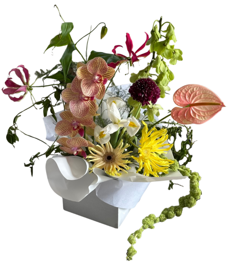 A floral arrangement featuring orchids, daisies, anthuriums, and other colorful flowers in a white paper-wrapped container.