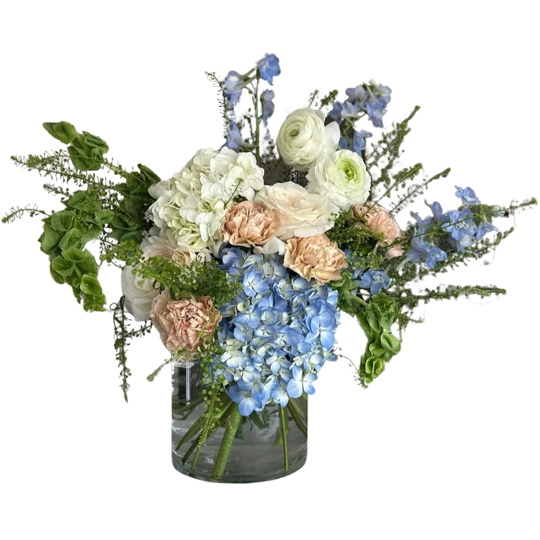 A bouquet of flowers in a glass vase featuring white, pink, and blue flowers with green foliage.