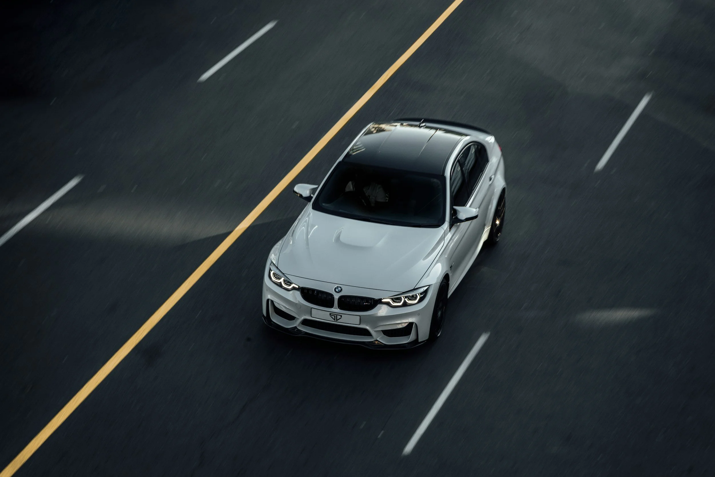 A white BMW sports car with a black roof driving on a multi-lane road at dusk or dawn.