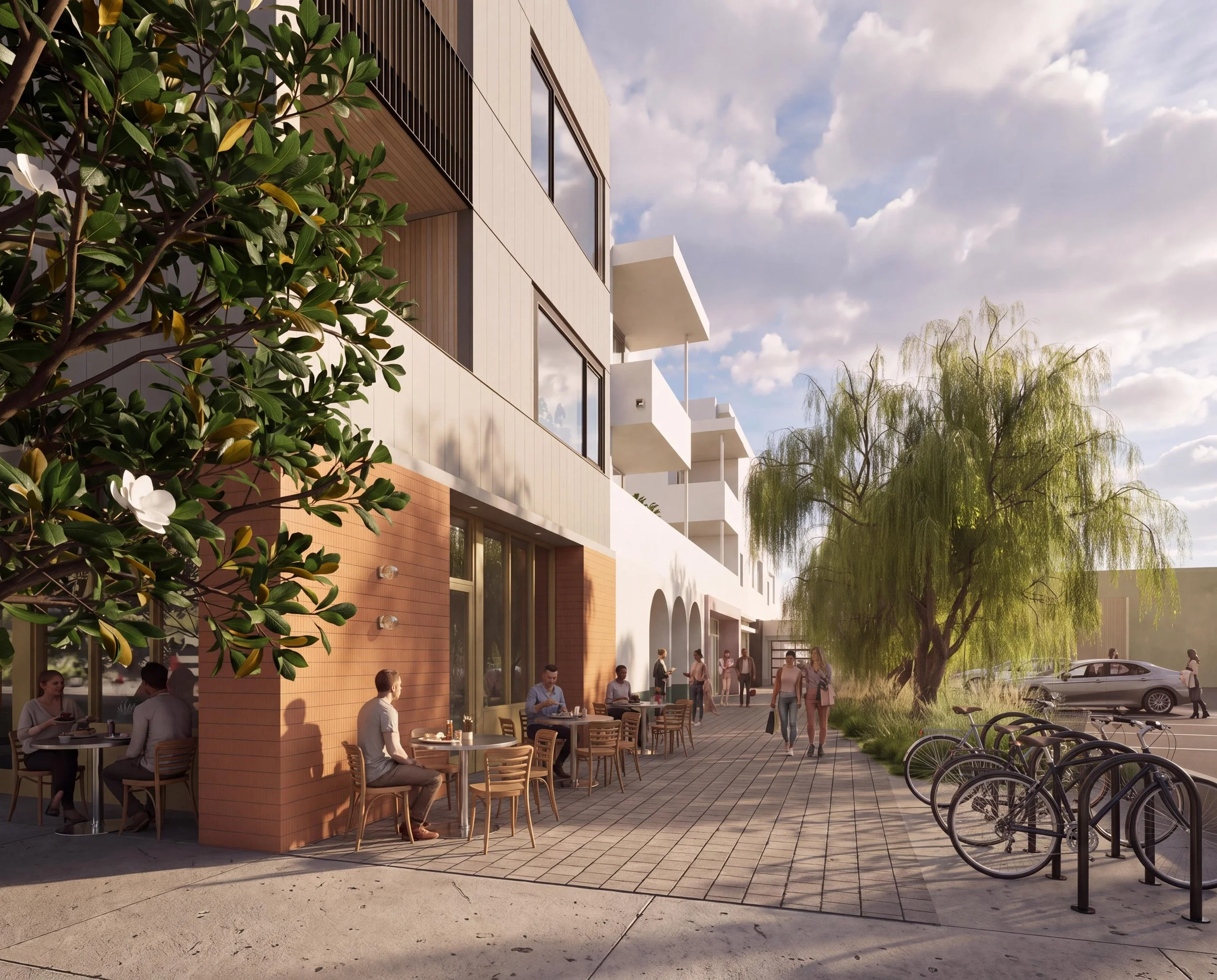 Outdoor cafe with people sitting at tables and socializing, modern apartment building with large windows and balconies, bicycles parked, lush trees, and a cloudy sky.