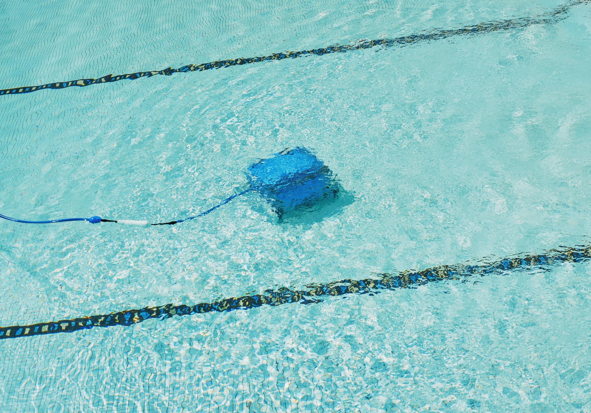 A blue robotic pool cleaner submerged in a swimming pool cleaning the tiled pool floor.