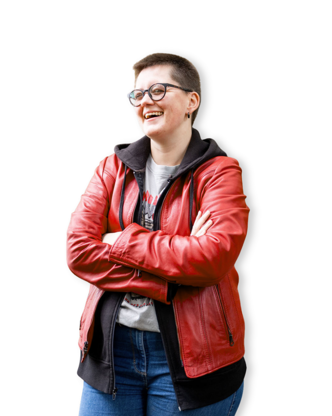 Junge erwachsene Person mit kurzen Haaren, Brille, roter Lederjacke, schwarzem Hoodie, weißen T-Shirt und blauen Jeans, die lachend mit verschränkten Armen steht.