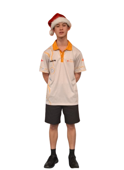 A young person wearing a Santa hat and a white polo shirt with orange details, standing with hands behind back.