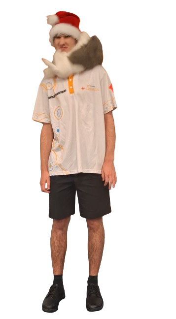 Person wearing a Santa hat, a beige scarf, a white short-sleeve shirt with colorful patterns, black shorts, and black shoes, standing with a neutral expression.