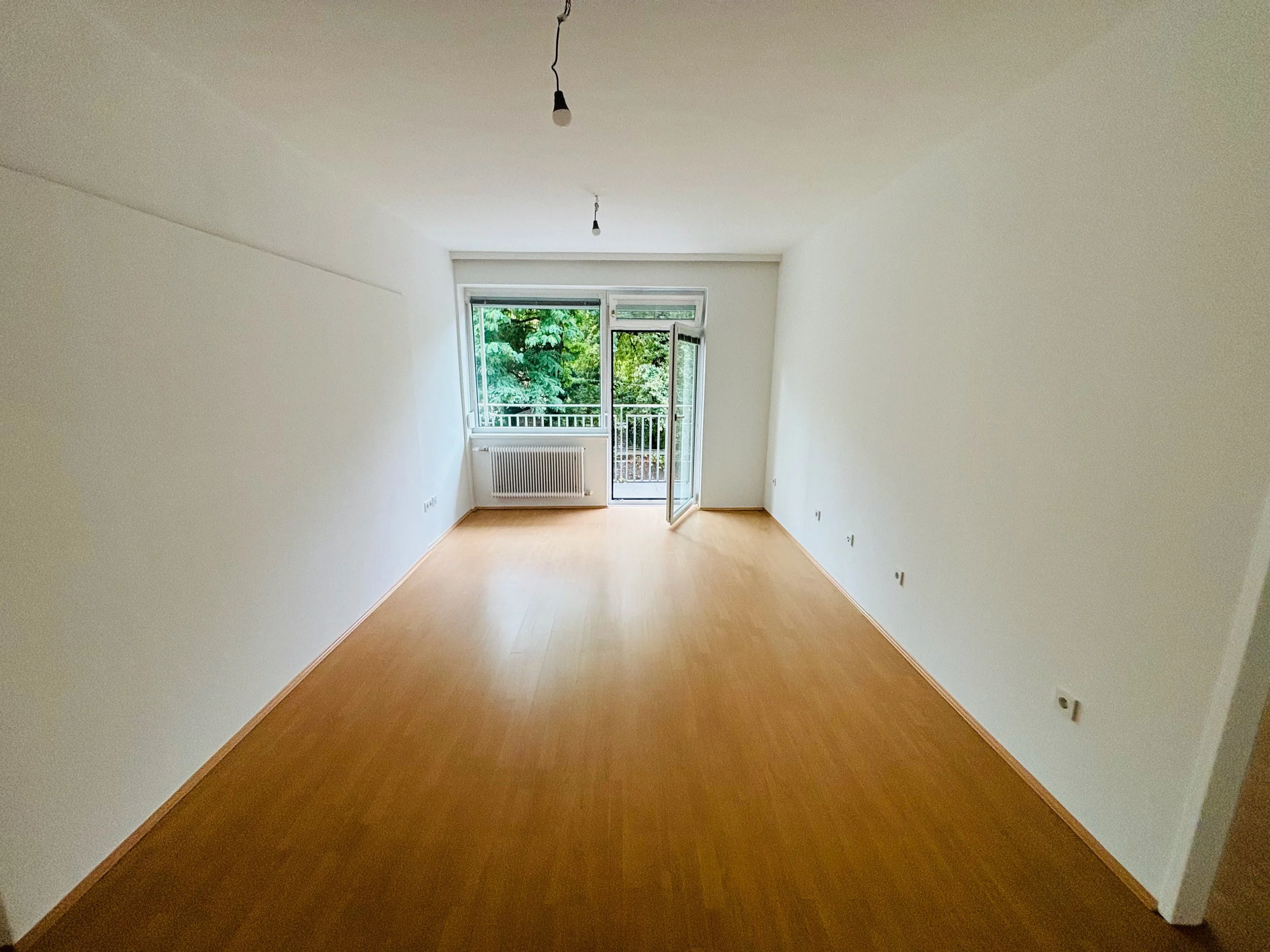 Leeres, gut beleuchtetes Wohnzimmer mit großen Fenstern und Balkonzugang.