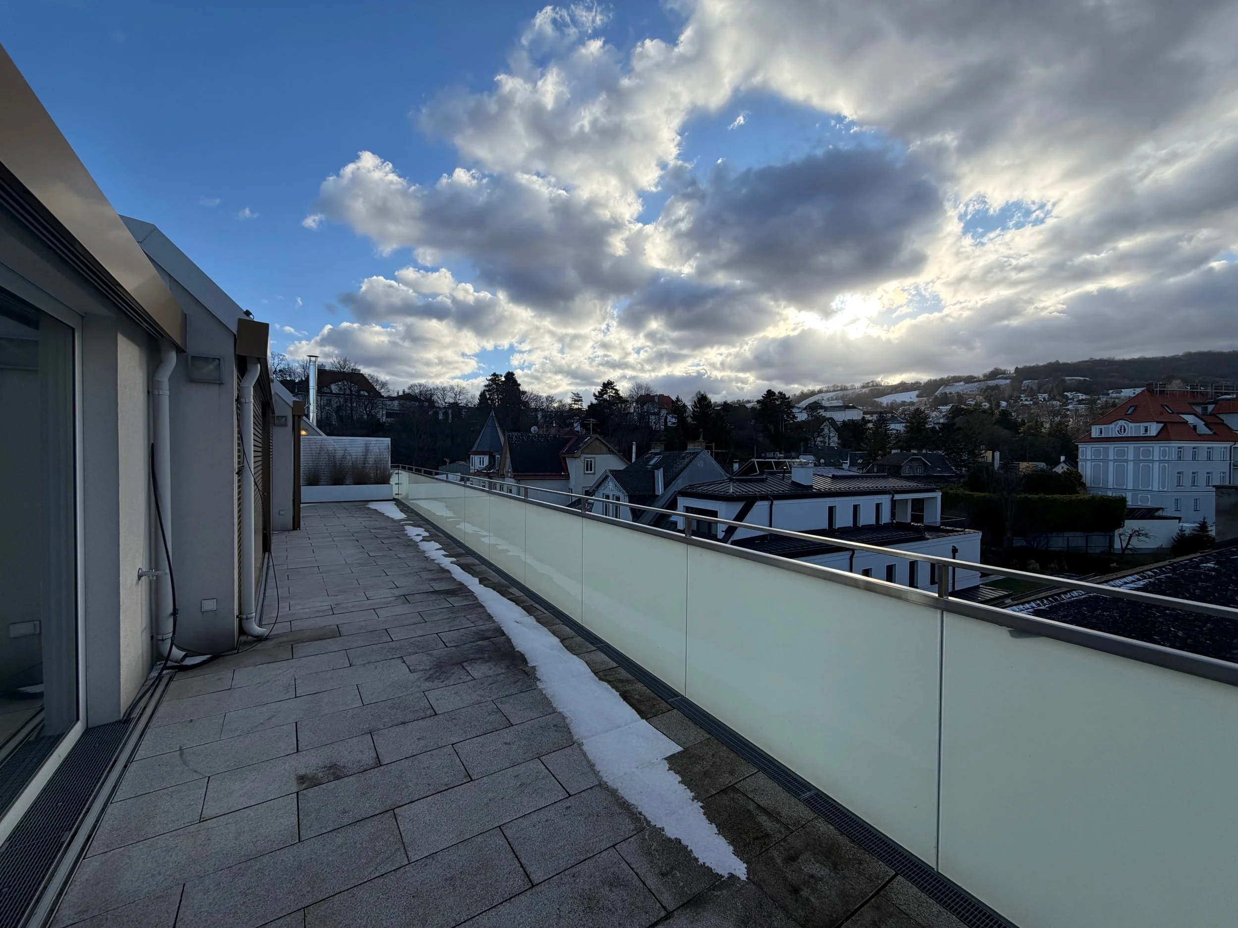 Balkon mit Glasgeländer und Häuser in einer ländlichen Gegend bei bewölktem Himmel