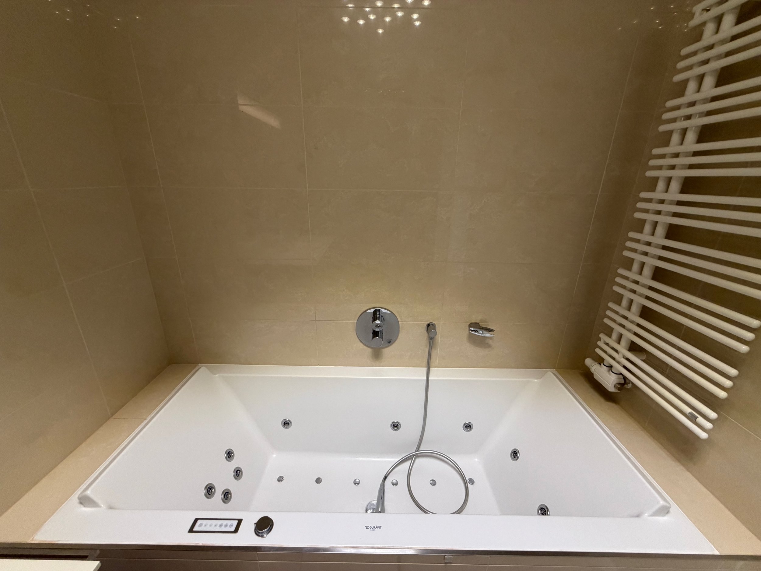 Ein moderner Whirlwanne mit Wasser, auf beige Fliesen und einem weißen Heizkörper