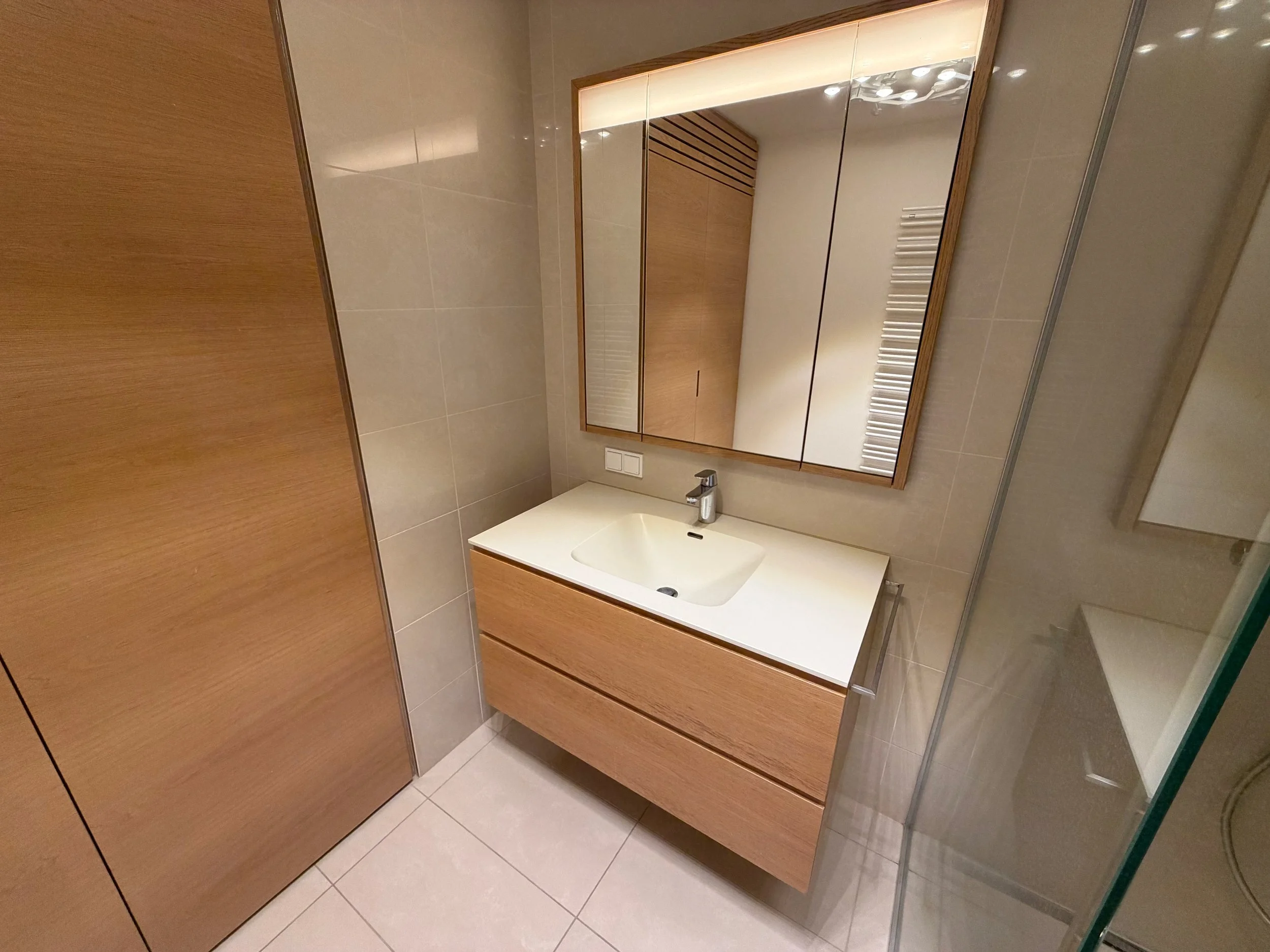 Modernes Badezimmer mit Holz- und Weißtönen, Waschbecken, Spiegel und reflekternder Glaswand.