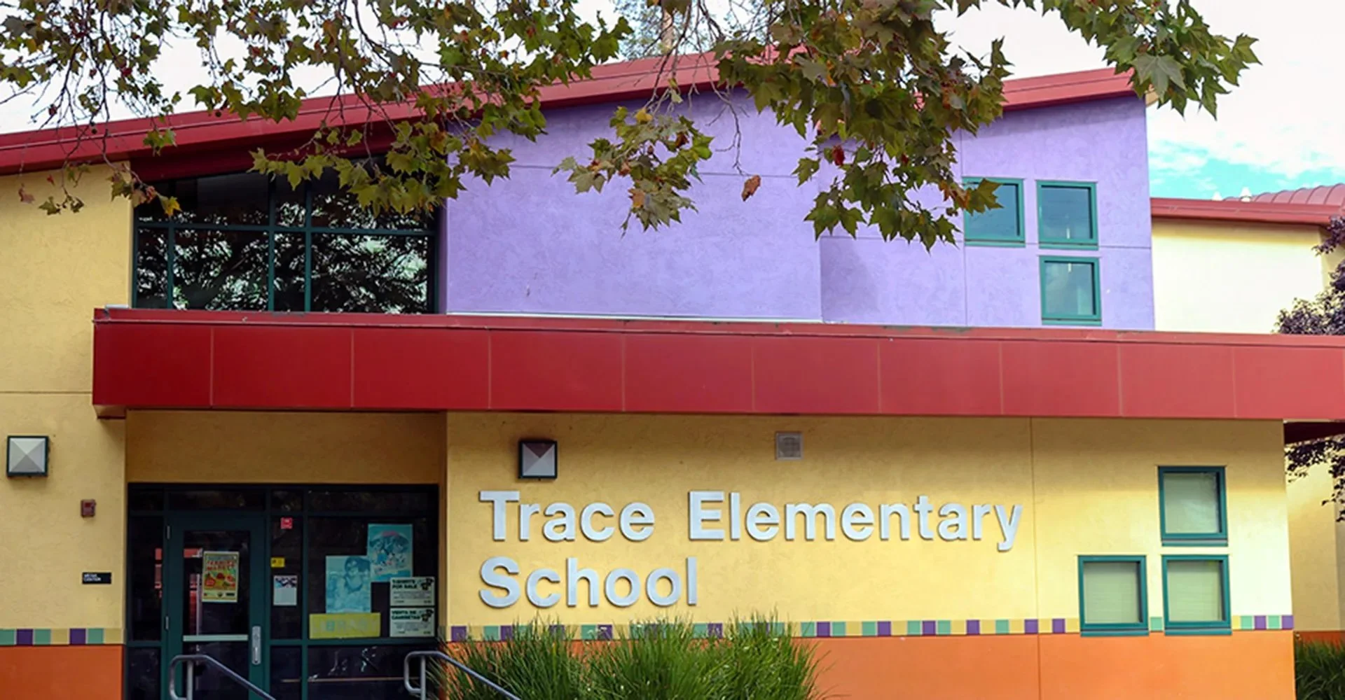 The front of Trace Elementary School with a yellow and purple exterior, red accents, and a sign displaying the school name.