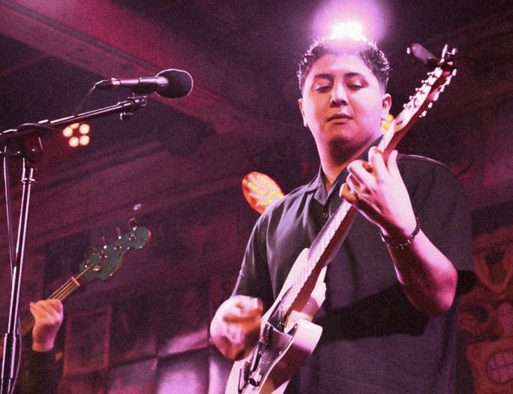 Musician playing electric guitar on stage with colorful lighting.