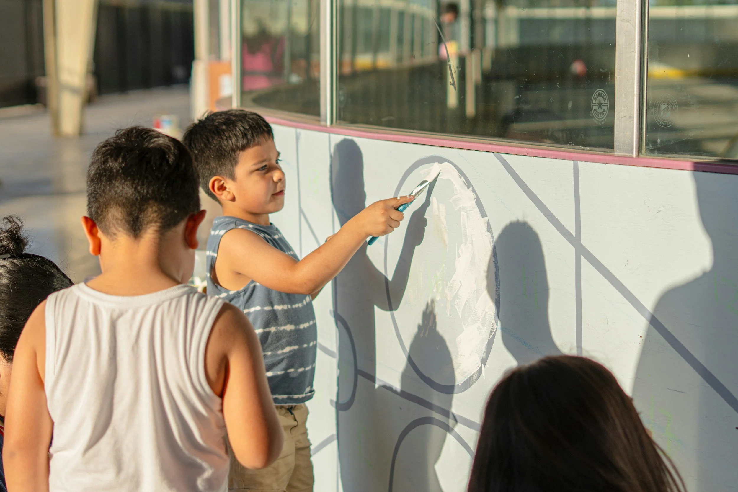 A boy painting a mural on a wall outside while other children watch.