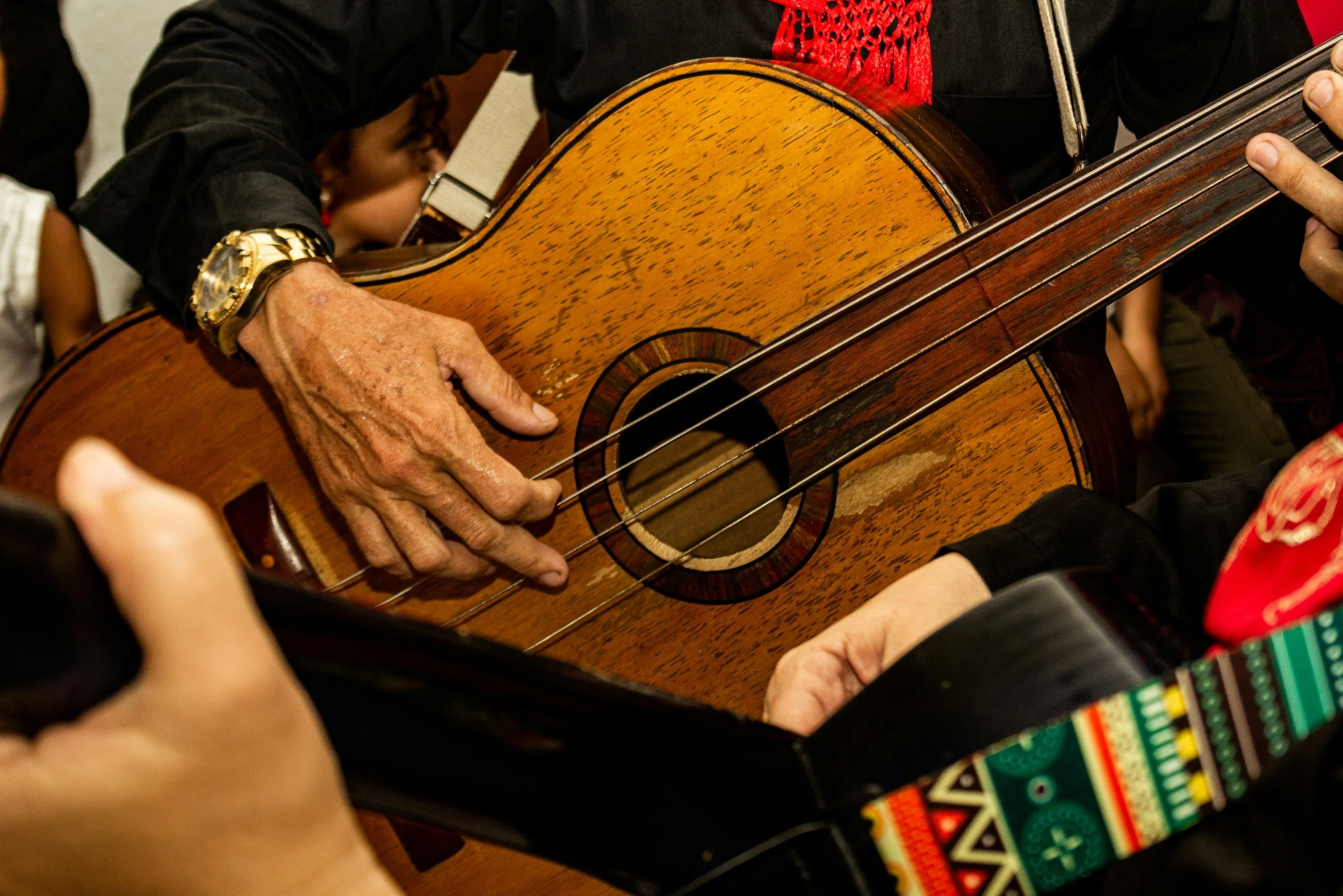 Close-up of hands playing a wooden acoustic guitar during a gathering.
