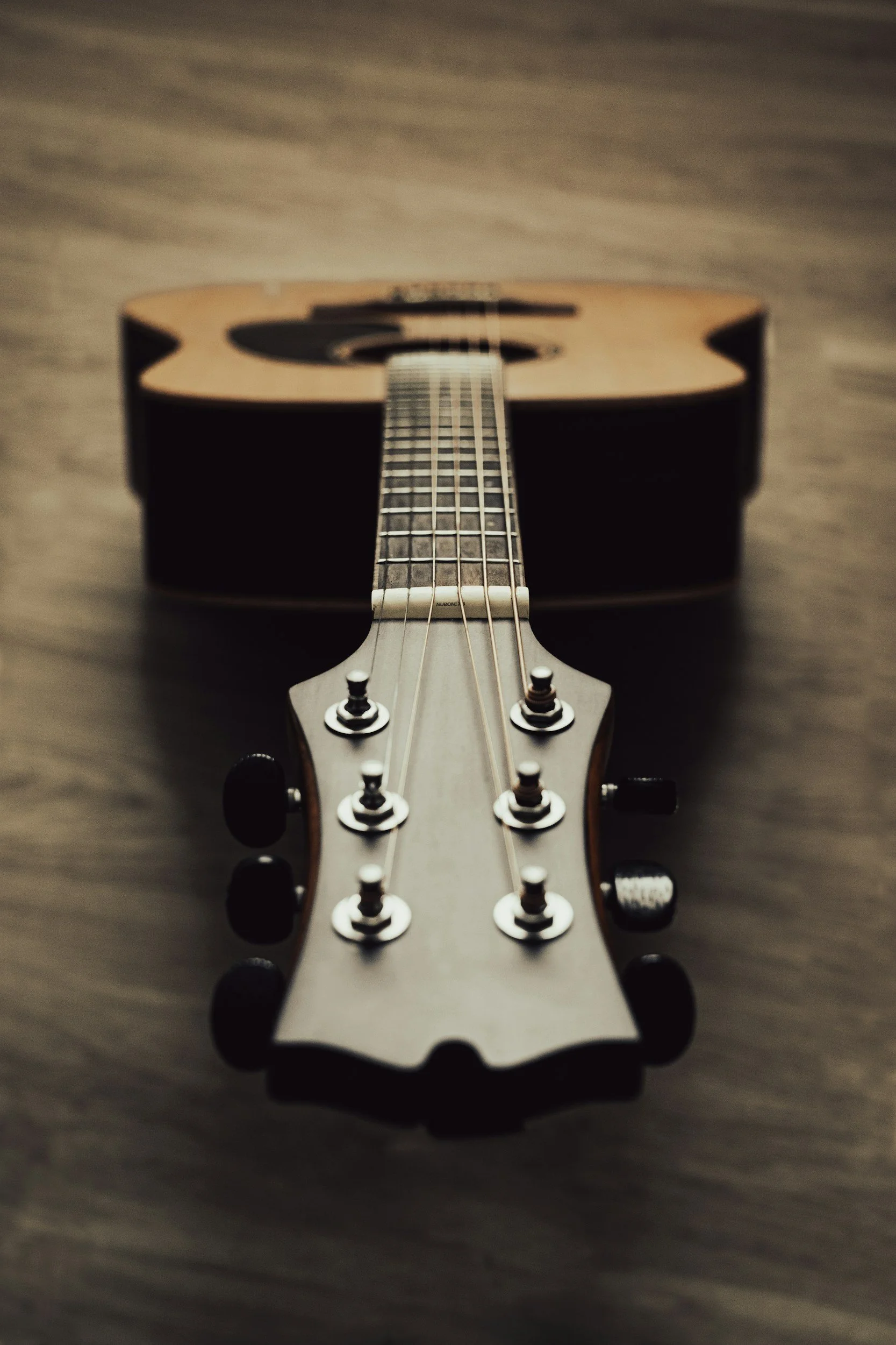 Close-up view of a guitar viewed from the headstock looking down the fretboard, with a blurred background.
