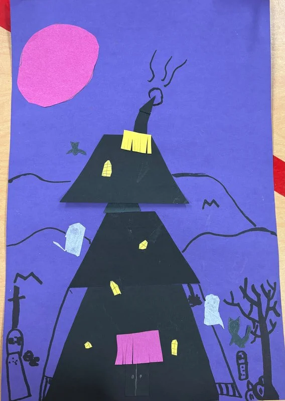Collage of a Halloween-themed scene with a black house made of paper cutouts stacked in a pyramid shape, with windows and doors, on a purple background. Features include a pink moon, small black cat, barren tree, and hills, with smoke coming from the