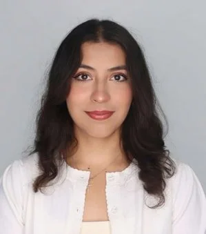 A young woman with long dark hair, wearing a white top, smiling softly against a light gray background.