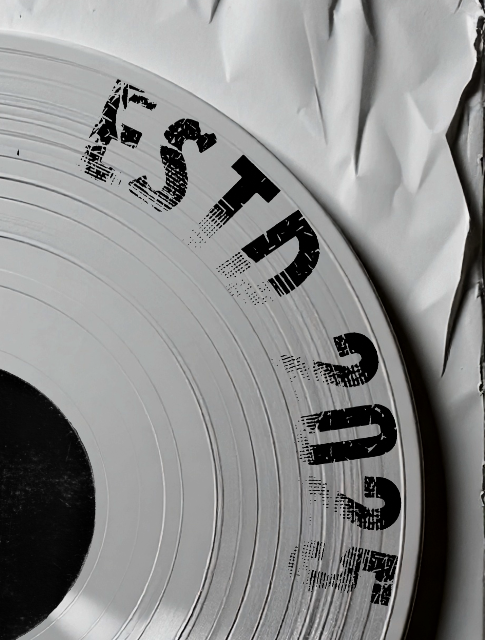 Close-up of a white vinyl record with black distress-style text and numbers, partially covered by crumpled white paper.