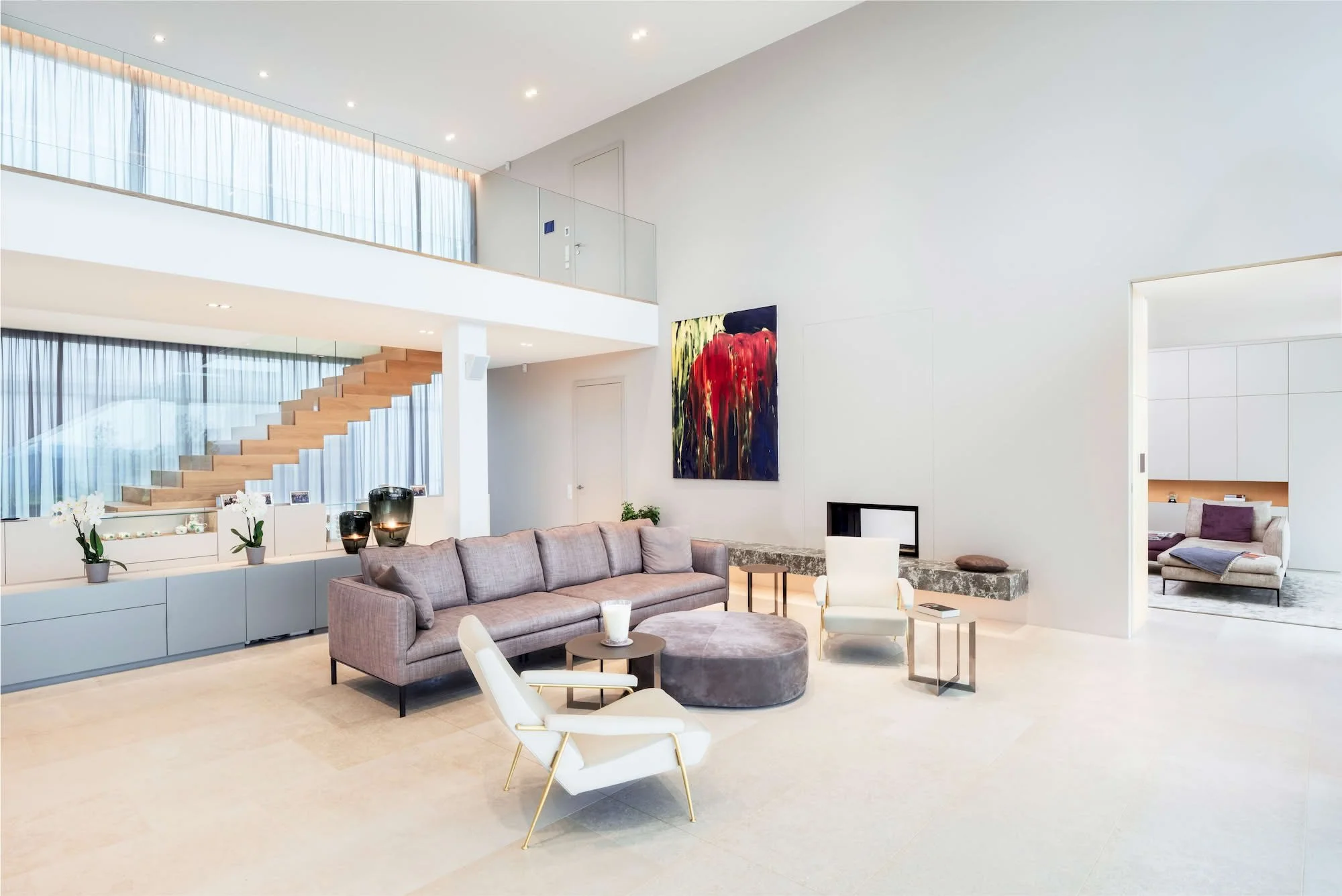 Modernes, offen gestaltetes Wohnzimmer mit hellem Mobiliar, Esstisch, Sofa, Wandkunst, Treppe im Hintergrund, viel natürlichem Licht durch große Fenster.