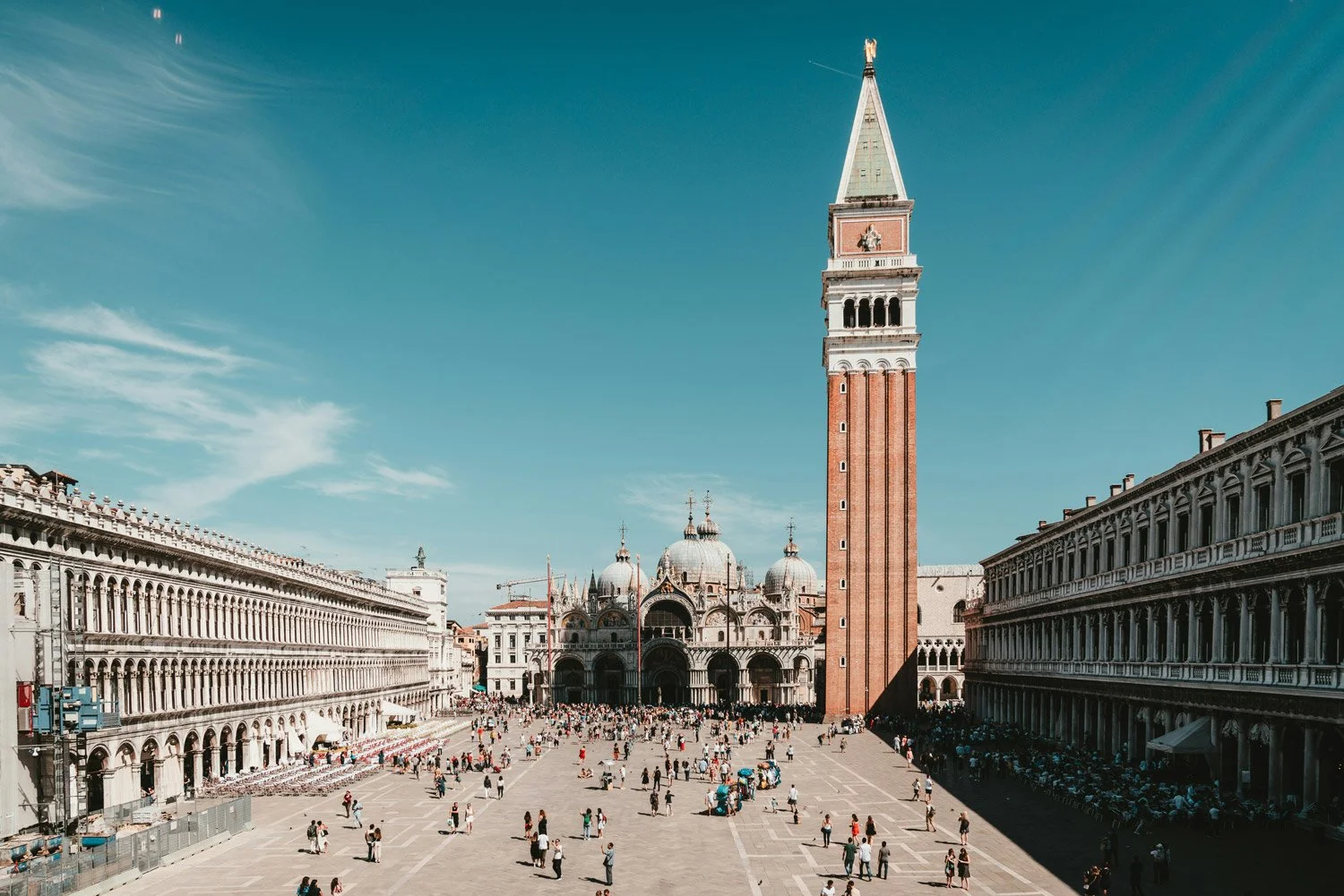 Der Markusplatz in Venedig mit dem Glockenturm, der basilica di San Marco im Hintergrund, und viele Menschen, die den Platz bevölkern, bei sonnigem Wetter.