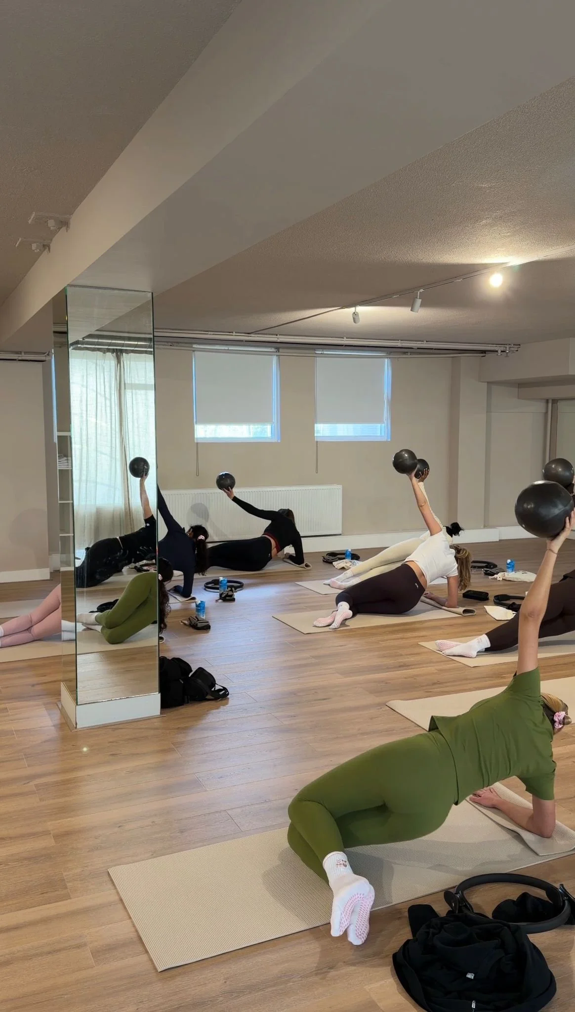 Group of women participating in a fitness class in a studio, lying on mats and lifting black exercise balls.