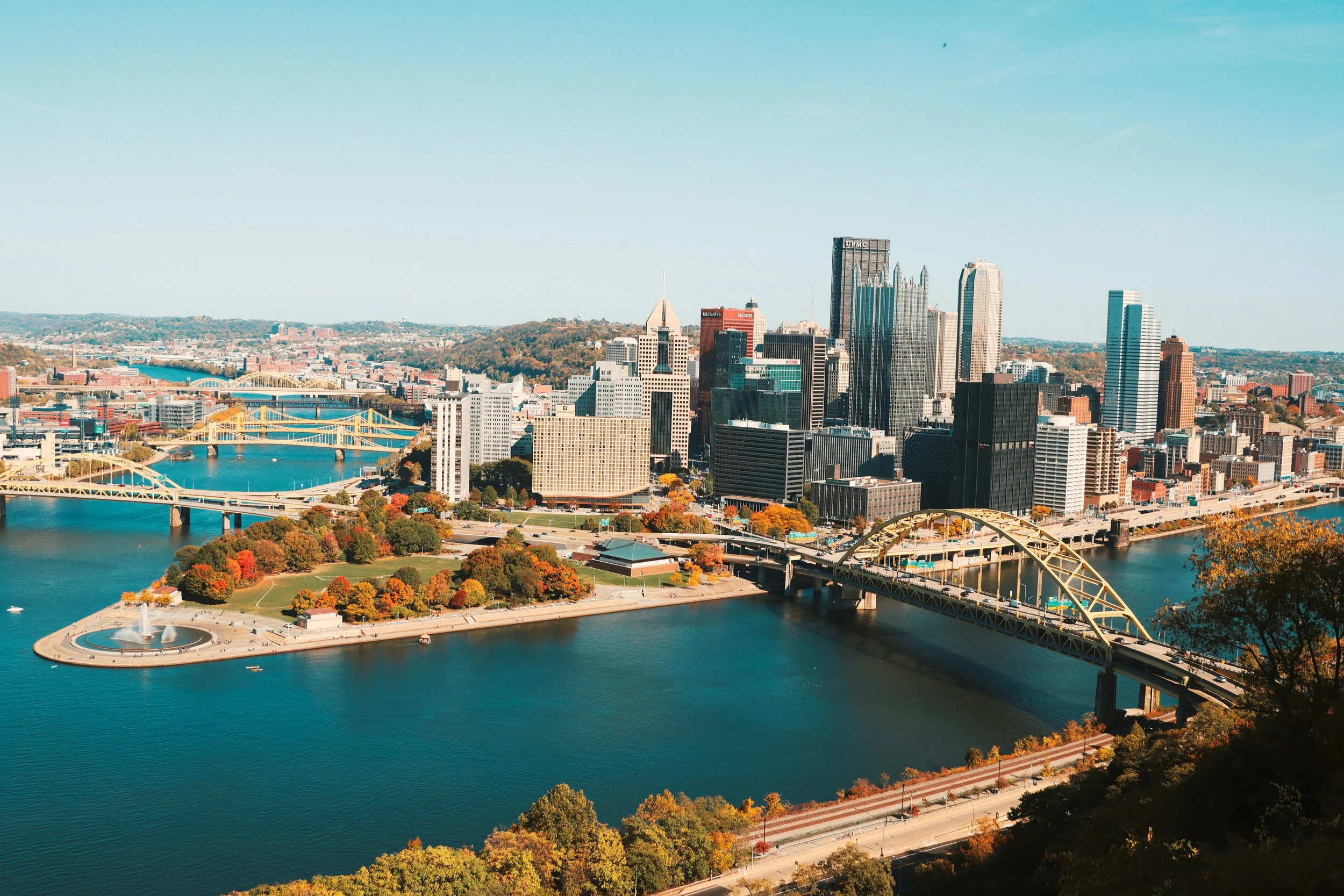 Aerial view of downtown Pittsburgh, Pennsylvania, featuring riverfront parks, bridges, and skyscrapers.
