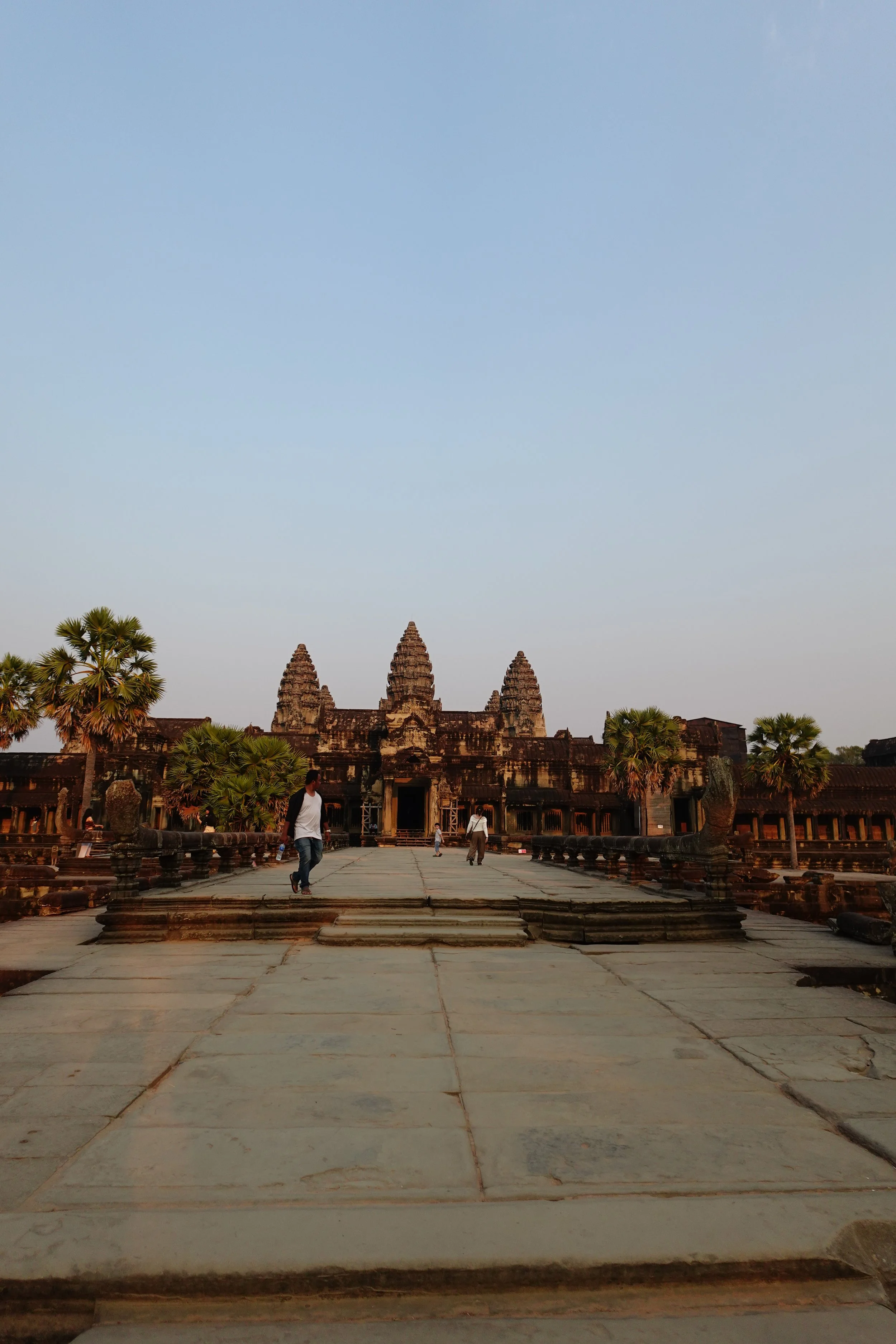Ancient temple with stone steps and a central entrance, surrounded by trees, under a clear sky.