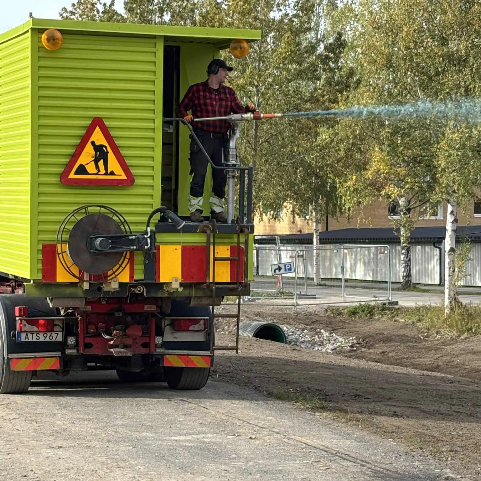 Man sprutar vatten från en hög ställning på en trafikutbildningsbil, som är grön med varningsskylt för vägjobb.