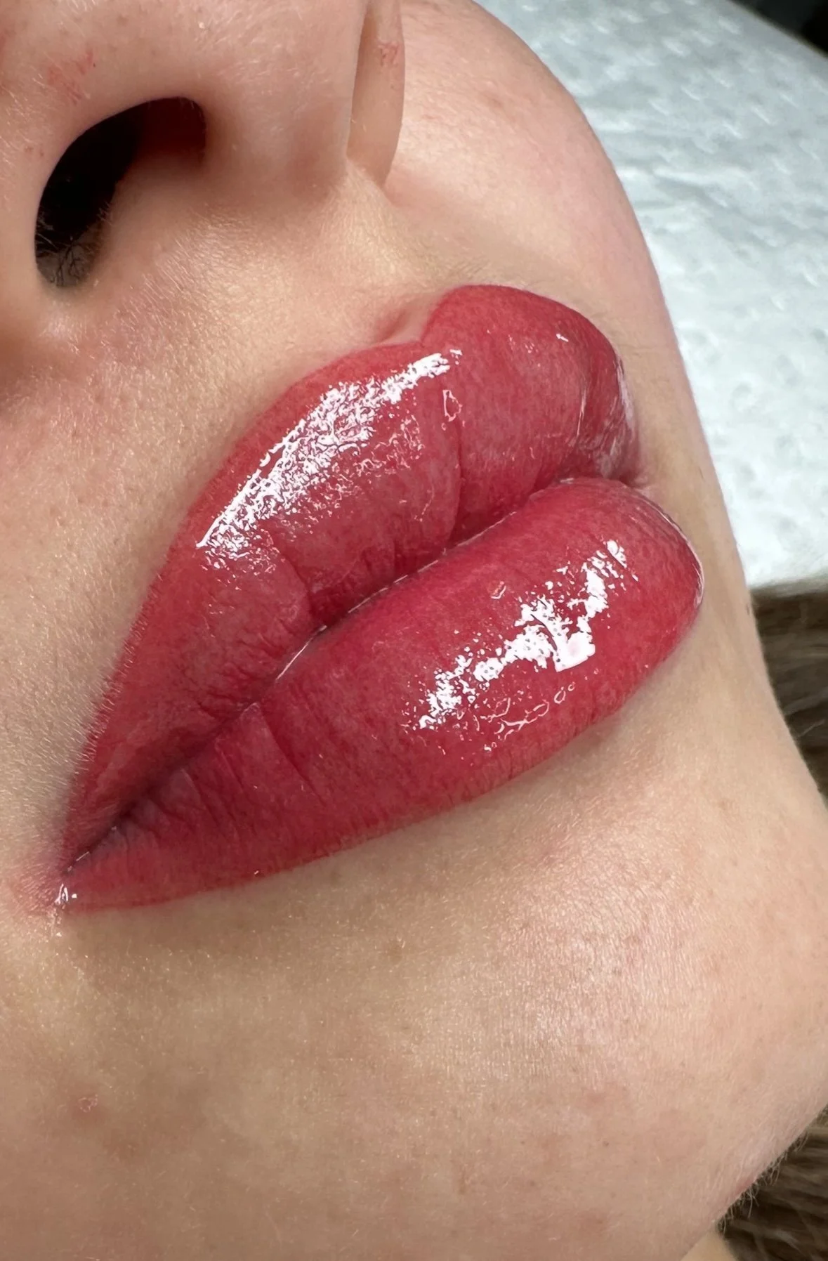 Close-up of a person's lips with shiny red lipstick, showing natural skin texture and a nearby nose.